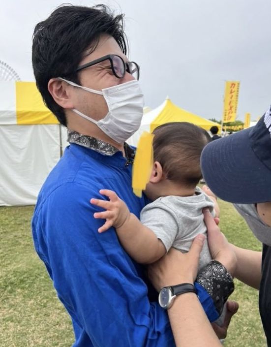 第一子を抱き上げるマスクを付けたマユリカ阪本の写真